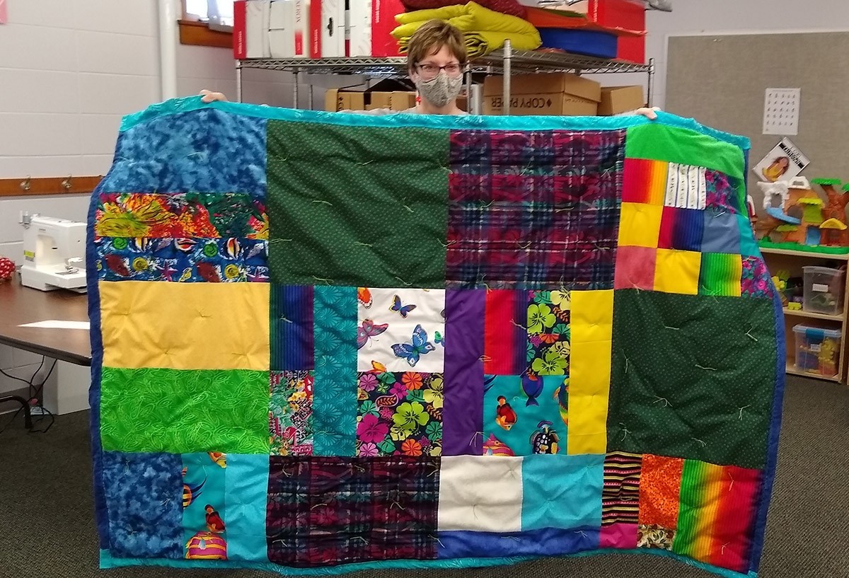 A woman holds up a colorful quilt