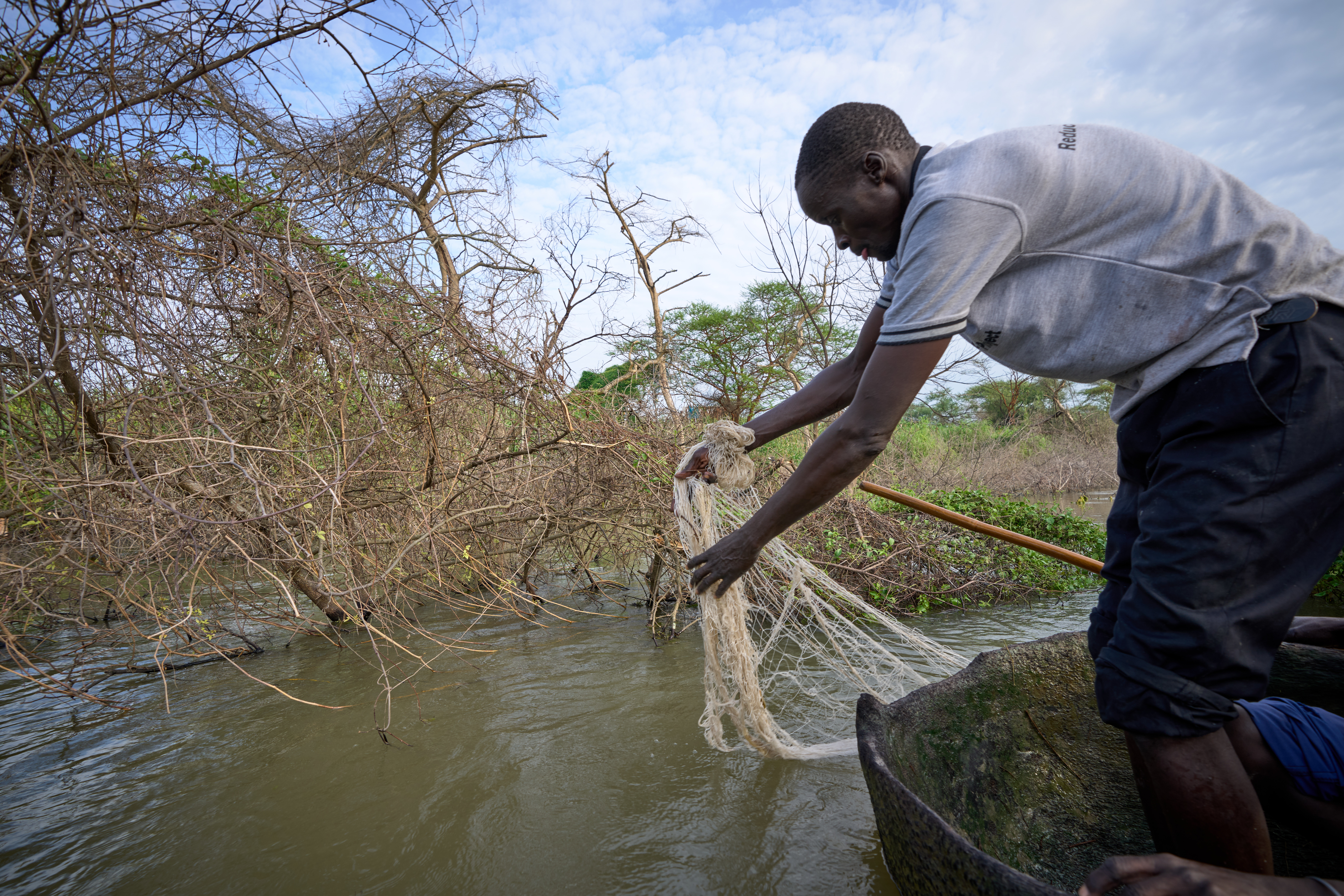 South Sudanese man casts a fishing net into a river as he stands in a canoe